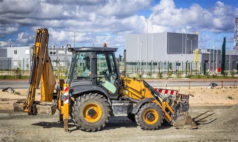Ilustracja pokazująca użycie wideł na przedniej łyżce koparko-ładowarki do transportu płyt drogowych