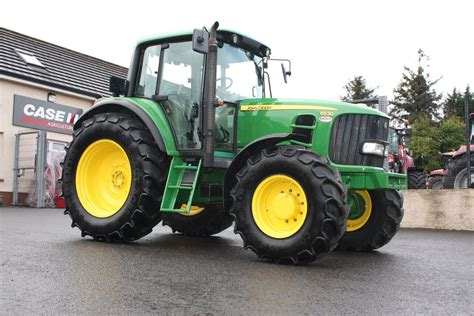 The John Deere 6530 tractor with a front loader at work on a farm field. High-resolution photo with clear details of the machinery and the agricultural environment.