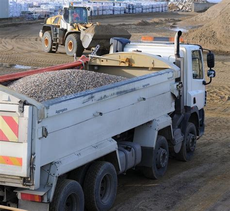 Zdjęcie przedstawiające nowoczesną wywrotkę podczas załadunku materiałów sypkich na placu budowy.