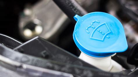 Infographics showing the typical location of the washer fluid reservoir under the hood, with a blue cap and a symbol.