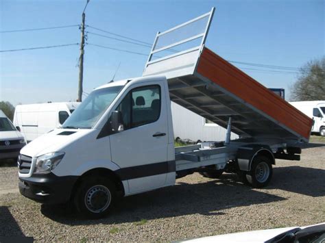 Thematic photo of a white or yellow tipper van (bus wywrotka) at a construction site or with a load of aggregate, against a Polish landscape.
