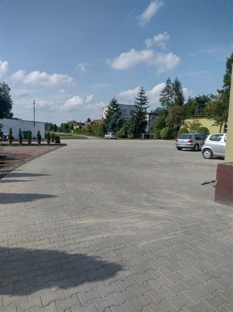 Zdjęcie przedstawiające zamiatarkę pracującą na placu parkingowym wyłożonym kostką brukową