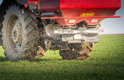 The Jar-Met SR1200 fertilizer spreader, showing its robust metal tank and dual-disc spreading mechanism, possibly with an exploded view of acid-resistant components.