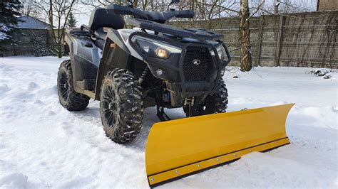 Quad z zamontowanym pługiem śnieżnym, w tle zaśnieżony krajobraz