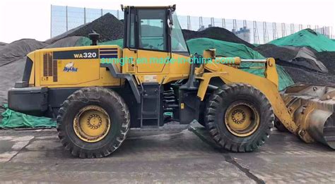 Thematic photo of a Komatsu WA320 wheel loader working with various attachments, including pallet forks.