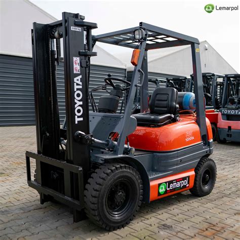 Grafika przedstawiająca kompaktowy, 3-kołowy wózek widłowy Toyota Traigo24 manewrujący w wąskim korytarzu magazynowym.