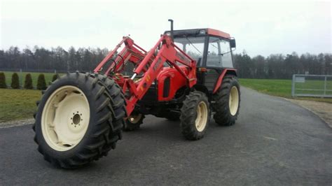 Ilustracja przedstawiająca nowoczesny ciągnik rolniczy z zamontowanym ładowaczem czołowym w akcji