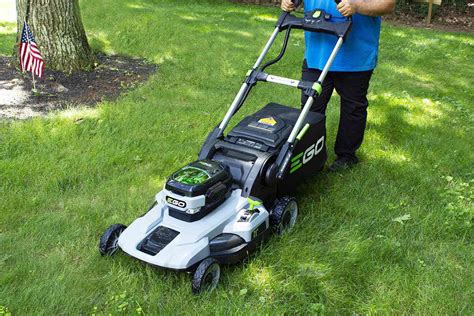 Thematic photo of a person mowing a lawn with a cordless lawn mower in a modern garden.