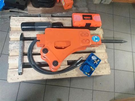Zdjęcie minikoparki wyposażonej w młot hydrauliczny podczas prac wyburzeniowych na placu budowy.