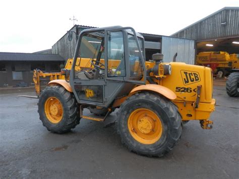 The JCB 526s telescopic loader working in a field with a bucket, demonstrating its versatility in agricultural tasks.