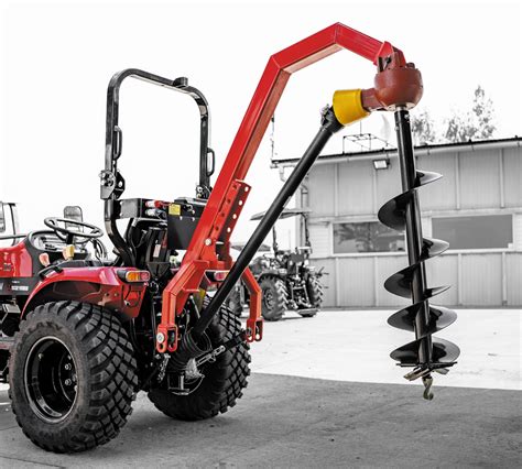 Wiertnica hydrauliczna podłączona do ciągnika rolniczego, wykonująca odwiert w ziemi.