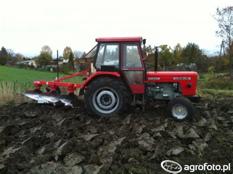 zdjęcie ciągnika z pługiem w trakcie orki, widoczne świeżo zaorane skiby