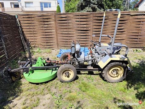 Mały traktorek z podłączoną kosiarką, pracujący na trawniku.