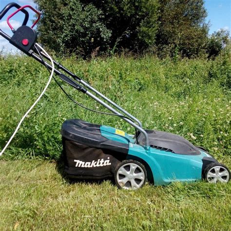 The Makita ELM3320 electric lawnmower in a garden setting, showing its compact design.