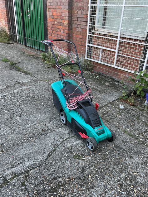 The John Gardener SHARP G83026 electric lawnmower in a garden setting, with its collection basket visible