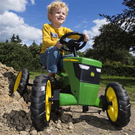 Dziecko jeżdżące na traktorku na pedały John Deere w ogrodzie