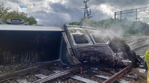 Zniszczony ciągnik siodłowy na torach kolejowych po zderzeniu z pociągiem, widoczne uszkodzenia obu pojazdów i rozrzucone fragmenty