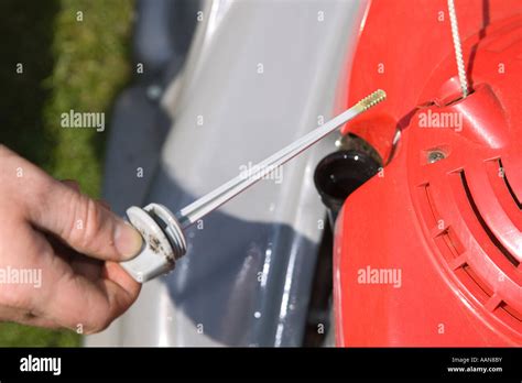 Thematic photo of a person preparing a lawnmower for the season, checking the oil level.