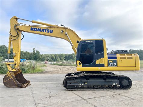 Zdjęcie przedstawiające koparkę gąsienicową Komatsu PC210 w trakcie pracy na placu budowy