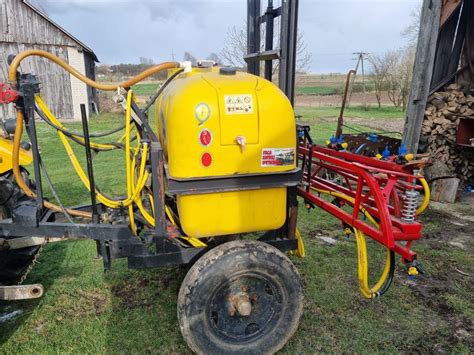 Zdjęcie przedstawiające opryskiwacz ciśnieniowy na kółkach w użyciu w profesjonalnym warsztacie samochodowym, np. podczas mycia podwozia.