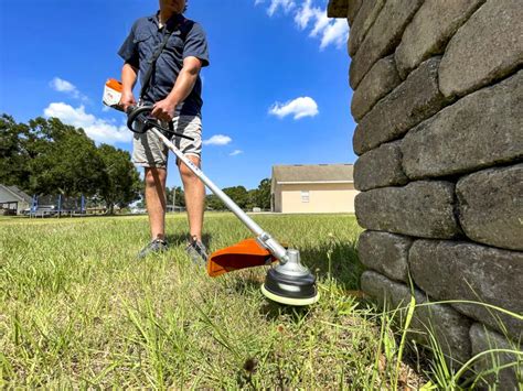 Thematic photo of a person mowing a lawn with a string trimmer, with emphasis on the fuel tank