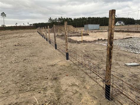 Zdjęcie: ogrodzenie w trakcie budowy, widoczne słupki i wykopy pod nie