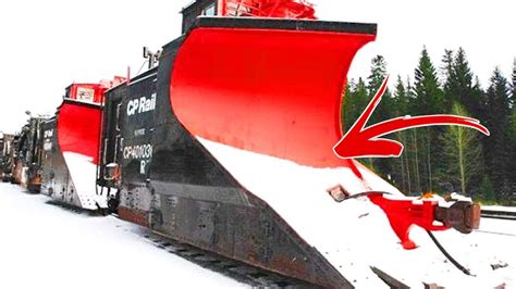 Ilustracja pociągu z pługiem śnieżnym odśnieżającego tory kolejowe, z elementami zimowego krajobrazu.