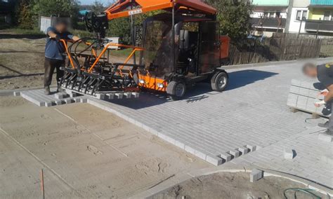 Ładowarka typu skid-steer podczas manewrowania z paletą kostki brukowej na placu budowy
