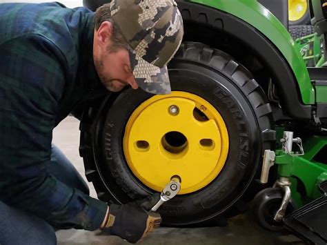 Thematic photo of a person working on a lawn tractor wheel, emphasizing safety gear