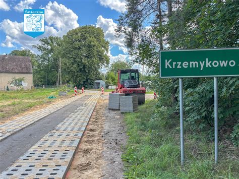 Szeroki widok na plac budowy drogi, gdzie operatorzy obsługują różnego rodzaju walce drogowe (statyczne, wibracyjne) przy układaniu nowej warstwy asfaltu.