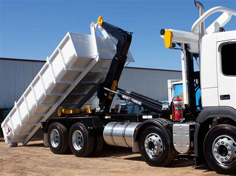 Thematic photo of a hooklift truck loading a container in an industrial or construction setting.