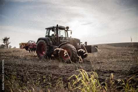 Fotografia dużego opryskiwacza polowego ciągnionego przez traktor na rozległym polu