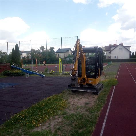 Zdjęcie placu budowy z pracującą koparko-ładowarką oraz wykopami przygotowanymi pod przyłącza