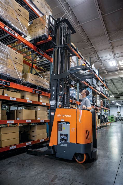 A Toyota Reach Truck (high-reach forklift) operating in a narrow aisle of a high-bay warehouse, stacking pallets.