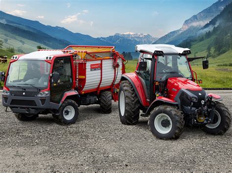 A Lindner Lintrac tractor working on a steep, grassy slope in the Alps, demonstrating its stability and specialized suspension system. The photo should show the unique design of the tractor adapted for mountain conditions.