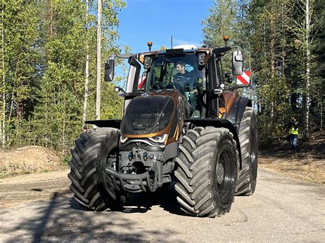 Zdjęcie ciągnika Valtra na drodze asfaltowej, otoczonego polami