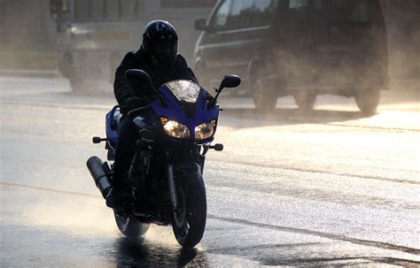 Motocyklista jadący po mokrej nawierzchni w lekkim deszczu
