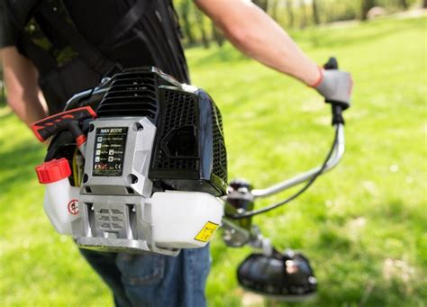 Zdjęcie kosy spalinowej NAX 800B w akcji, tnącej trawę przy ogrodzeniu