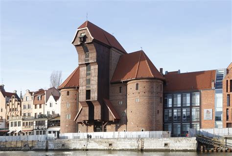 Widok panoramiczny na Żuraw Gdański od strony Motławy z widoczną drewnianą konstrukcją dźwigową oraz ceglanymi basztami.