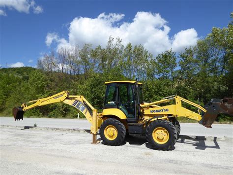 detalne zdjęcie ramienia koparki Komatsu WB 97 z widocznymi przewodami hydraulicznymi i oznakami zużycia