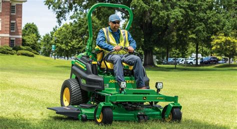Photo of a compact John Deere tractor mowing grass in a park or municipal area