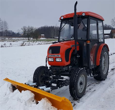 Zdjęcie ciągnika komunalnego wyposażonego w pług śnieżny i posypywarkę podczas pracy