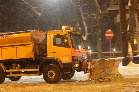 Zdjęcie przedstawiające akcję odśnieżania ulic w Zakopanem, pług spychający śnieg na pobocze lub ładowarkę ładującą śnieg na wywrotkę.