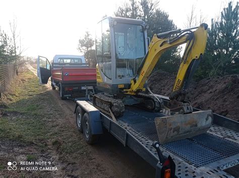 Zdjęcie placu budowy z pracującą minikoparką i wywrotką w tle