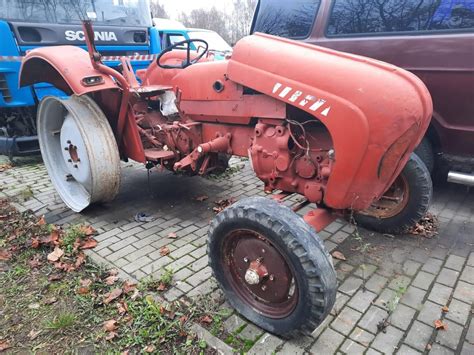 Zdjęcie przedstawiające odrestaurowany, zabytkowy ciągnik w otoczeniu wiejskiego krajobrazu.