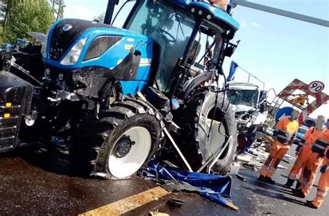 Zdjęcie miejsca wypadku przedstawiające zniszczony ciągnik rolniczy na poboczu i busa z uszkodzonym przodem na jezdni.