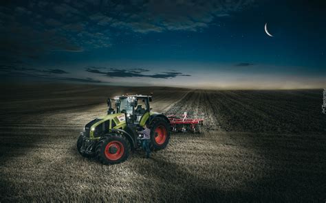 ciągnik pracujący w polu nocą, oświetlony światłami, unoszący lekki kurz