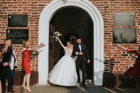 zdjęcie pary młodej wychodzącej z kościoła, obsypywanej płatkami kwiatów i ryżem