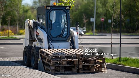 Thematic photo of a tractor with a front loader working on a paved area, unloading pallets or sweeping