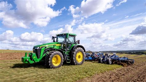 Tematyczne zdjęcie czarnego ciągnika John Deere 8R 340 pracującego w polu z czarnym pługiem